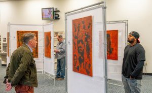 Three men look at artwork during an exhibit at the library.